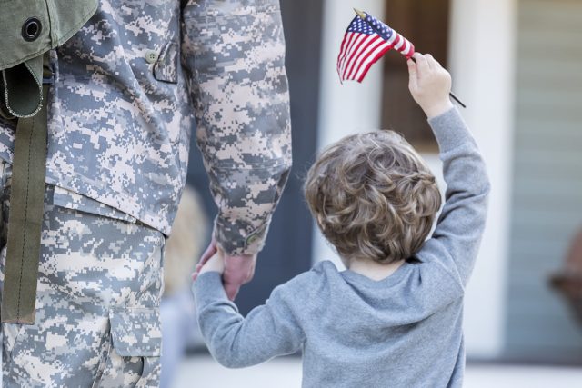 Rear view of boy holding hands with military dad